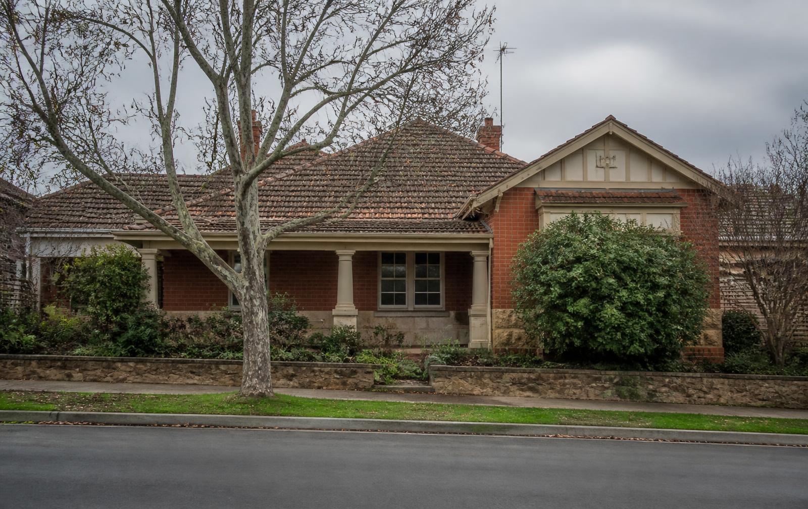 Established red-brick Australian home on a quiet suburban street under overcast skies